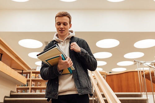 Young man with bag in library. Male student heading for class holding books.