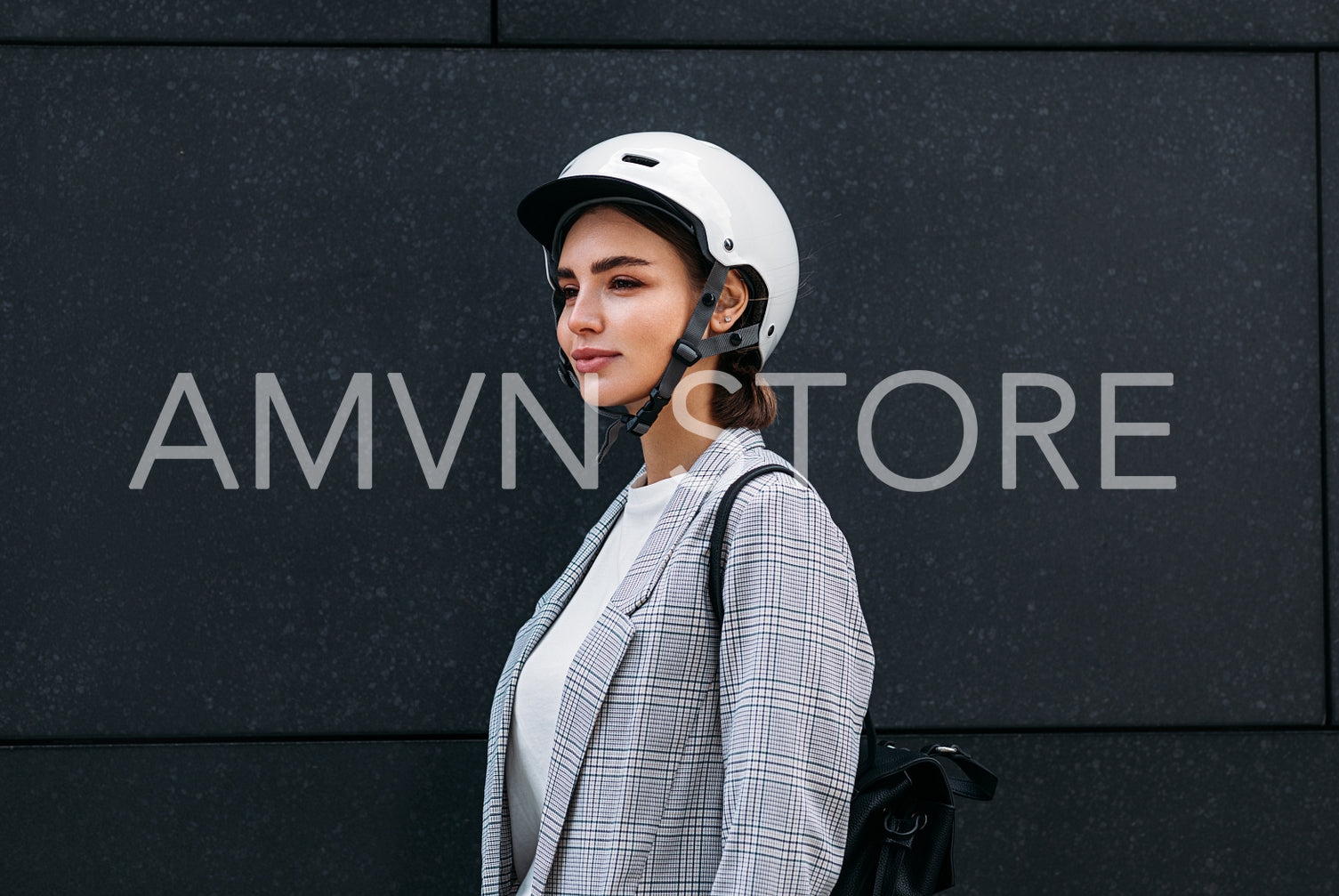 Businesswoman in white cycling helmet wearing backpack standing against a black wall outdoors