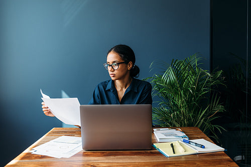 Serious businesswoman sitting by a desk and holds documents