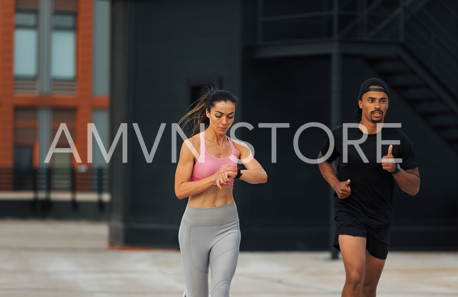 Two athletes sprinting on a rooftop. Young woman checking fitness tracker while running.