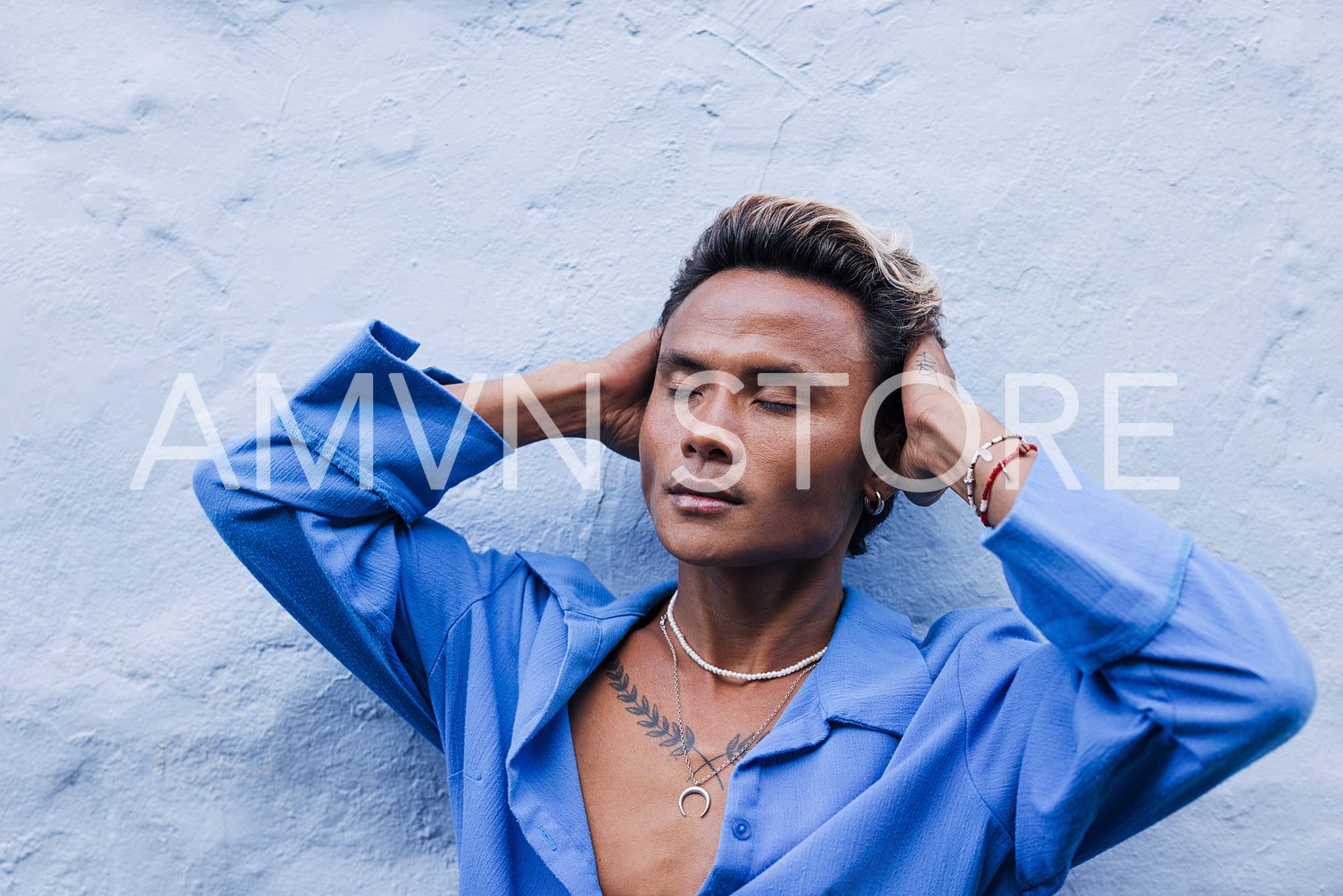 Stylish guy in a blue shirt leaning on a wall touching his head with closed eyes