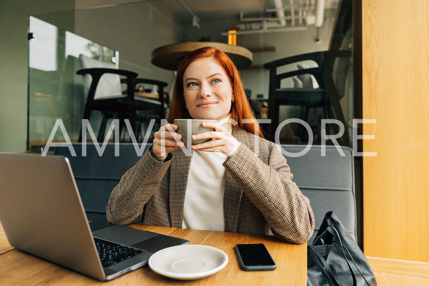 Smiling redhead woman in formal wear drinking coffee looking at window in cafe