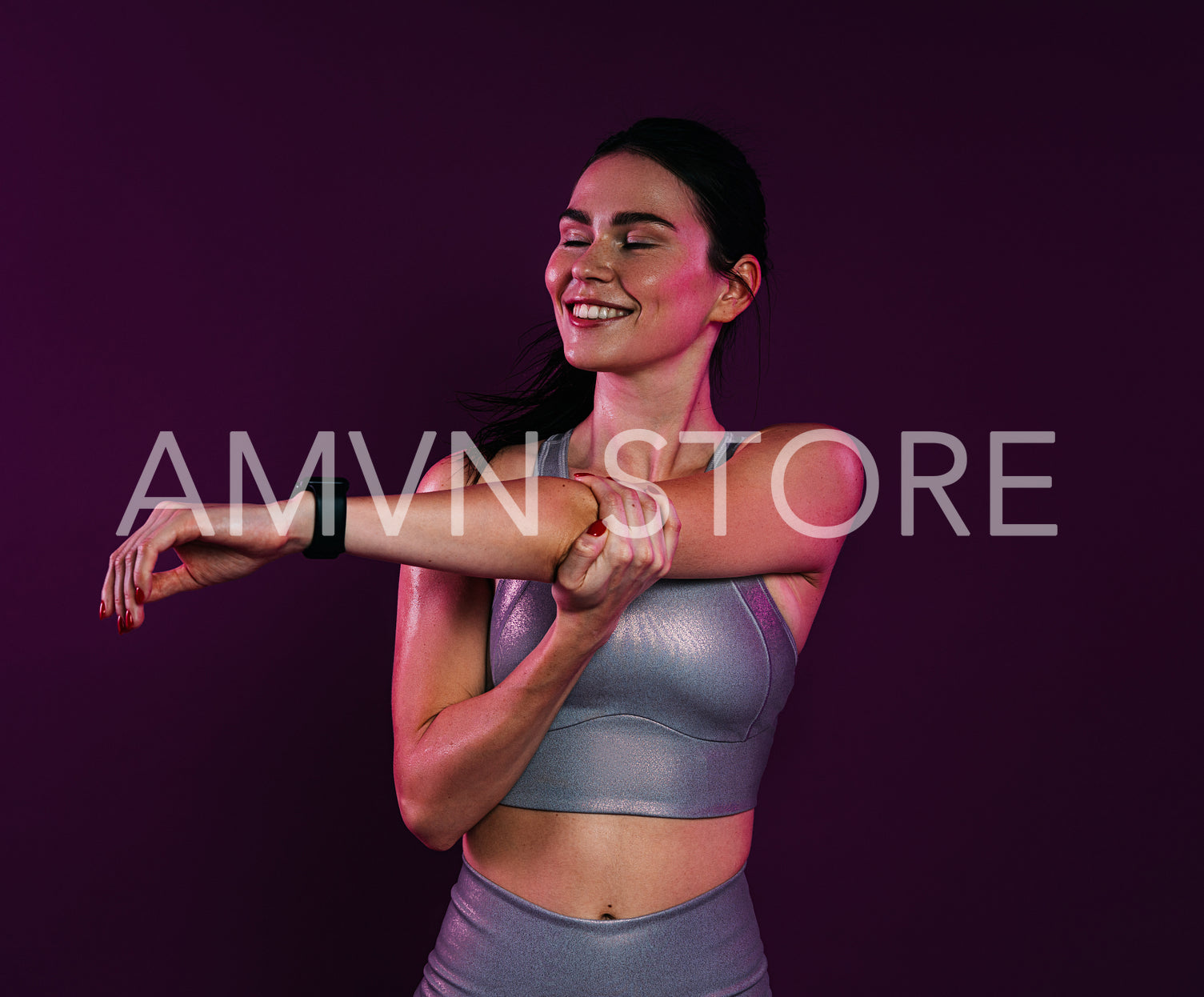 Young smiling female with closed eyes stretching and flexing her hands over magenta background in studio