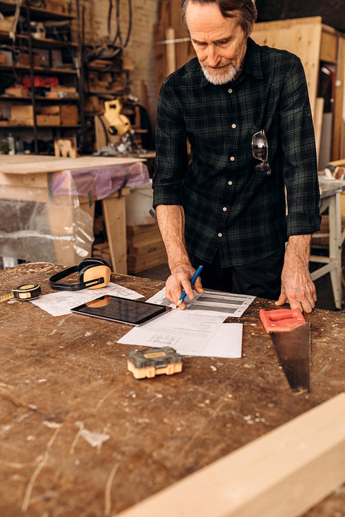 Mature man checking drawing before starting his work at a carpentry workshop