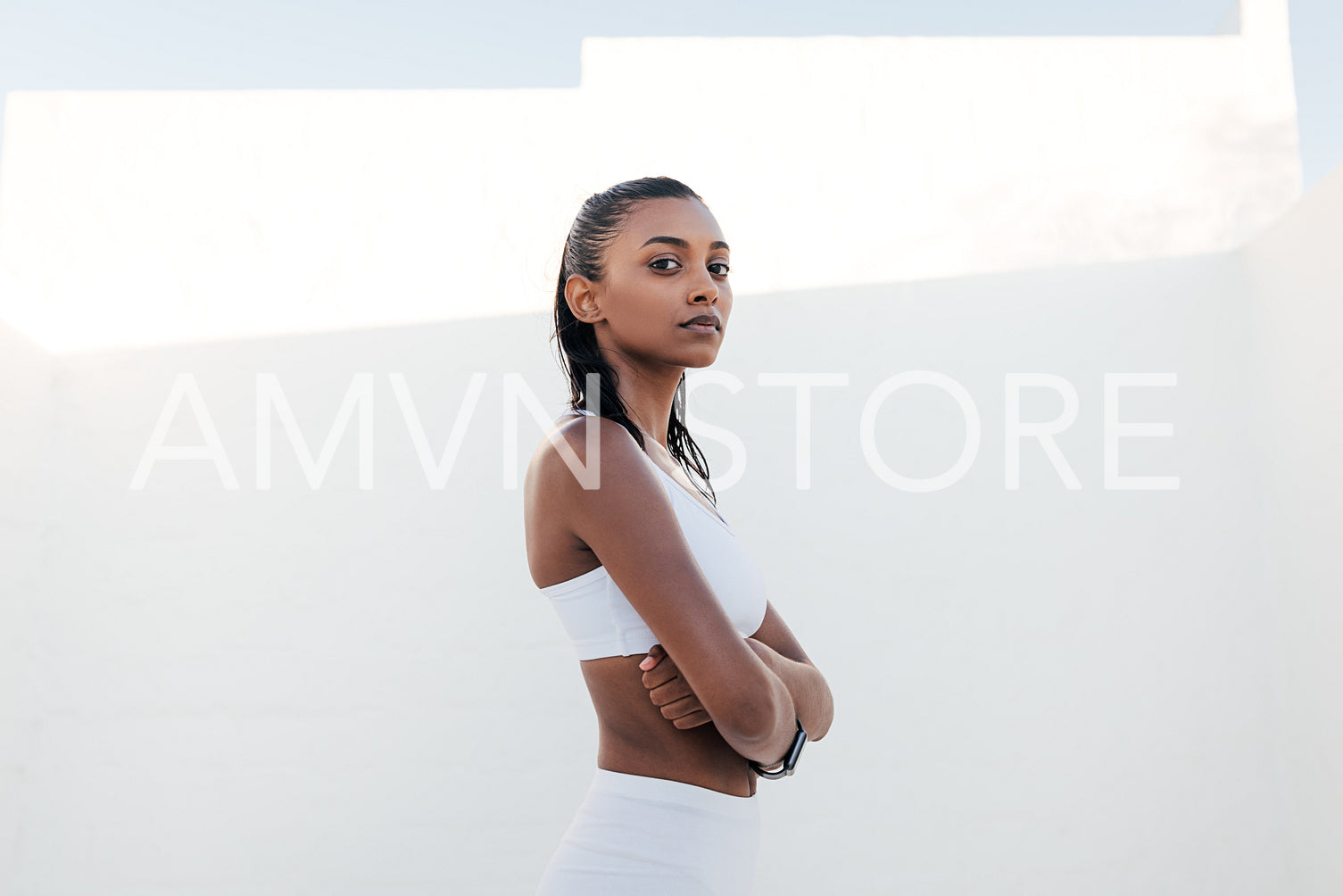 Confident woman in a white sports bra standing with crossed hands and looking at the camera