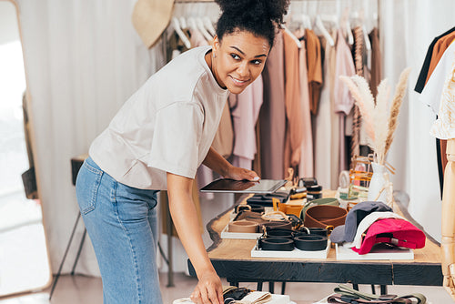 Woman working in her local clothes store. Boutique owner checking accessories holding digital tablet.