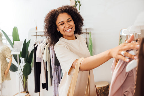 Portrait of a happy woman looking for new clothes standing at rack in small shop