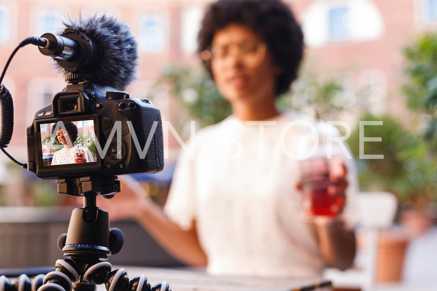 Woman with a juice in one hand talking to digital camera. Vlogger recording content.	