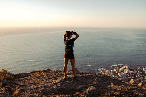 Rear view of young woman looking on the ocean from mountain top after hike