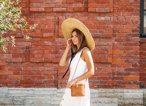 Side view of a young stylish woman in a big hat walking on the city street