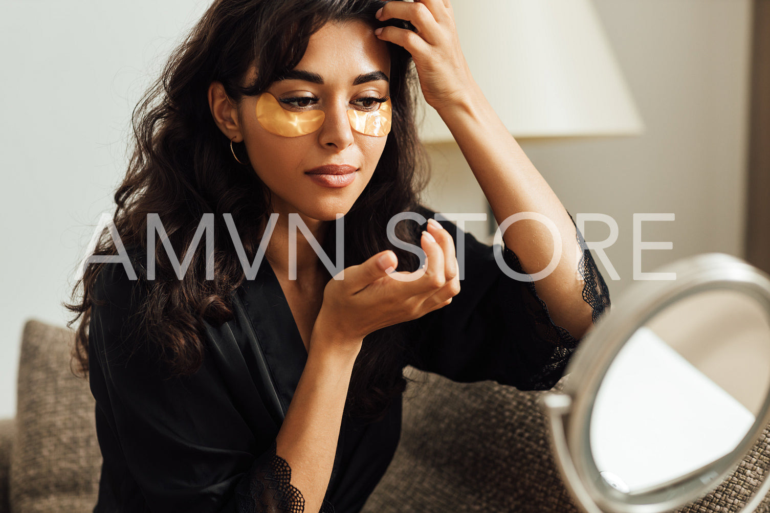 Woman in satin robe looking at mirror and applying face patch in room	