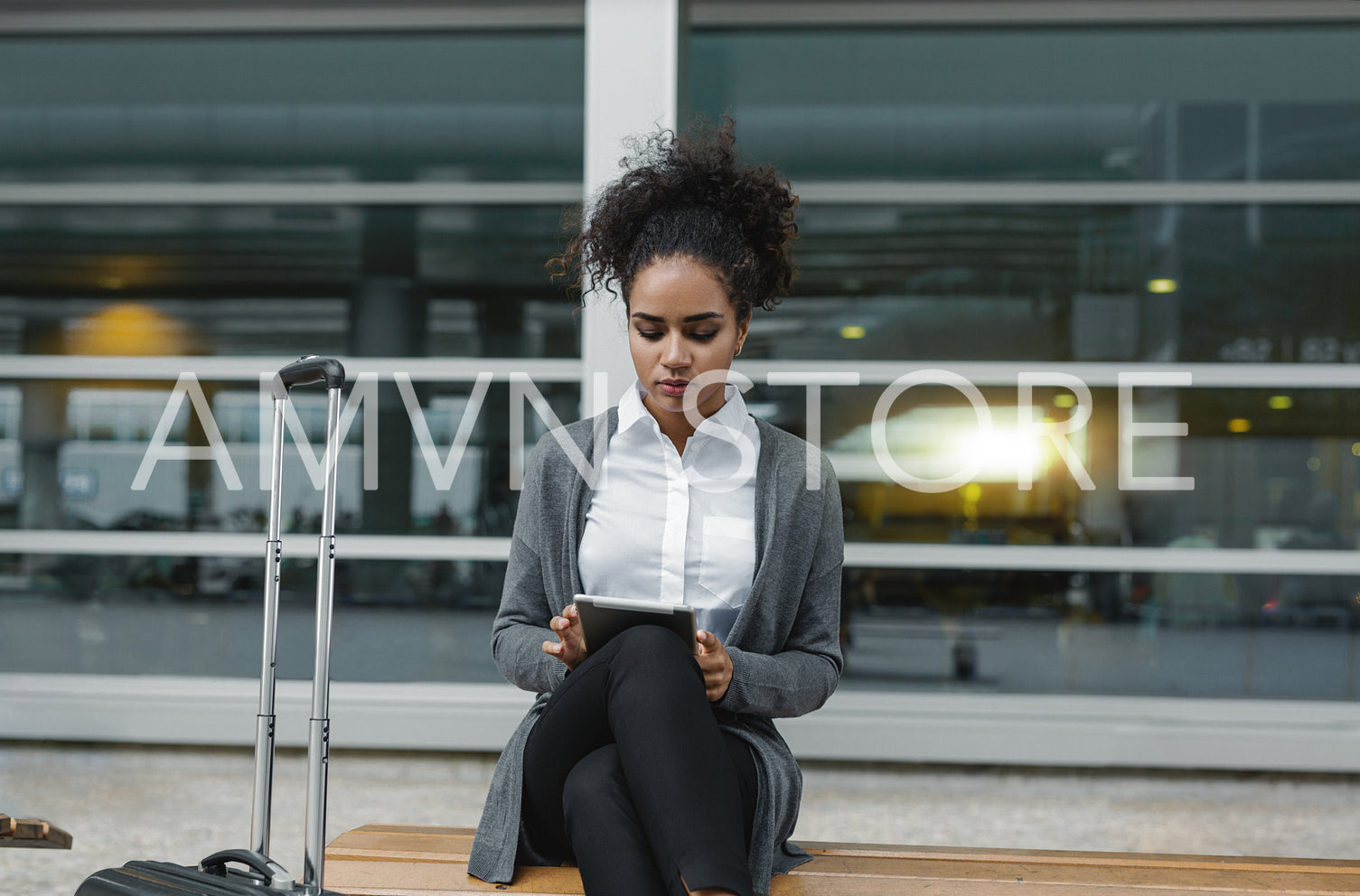 Young businesswoman working on her digital tablet, sitting on bench near public building	