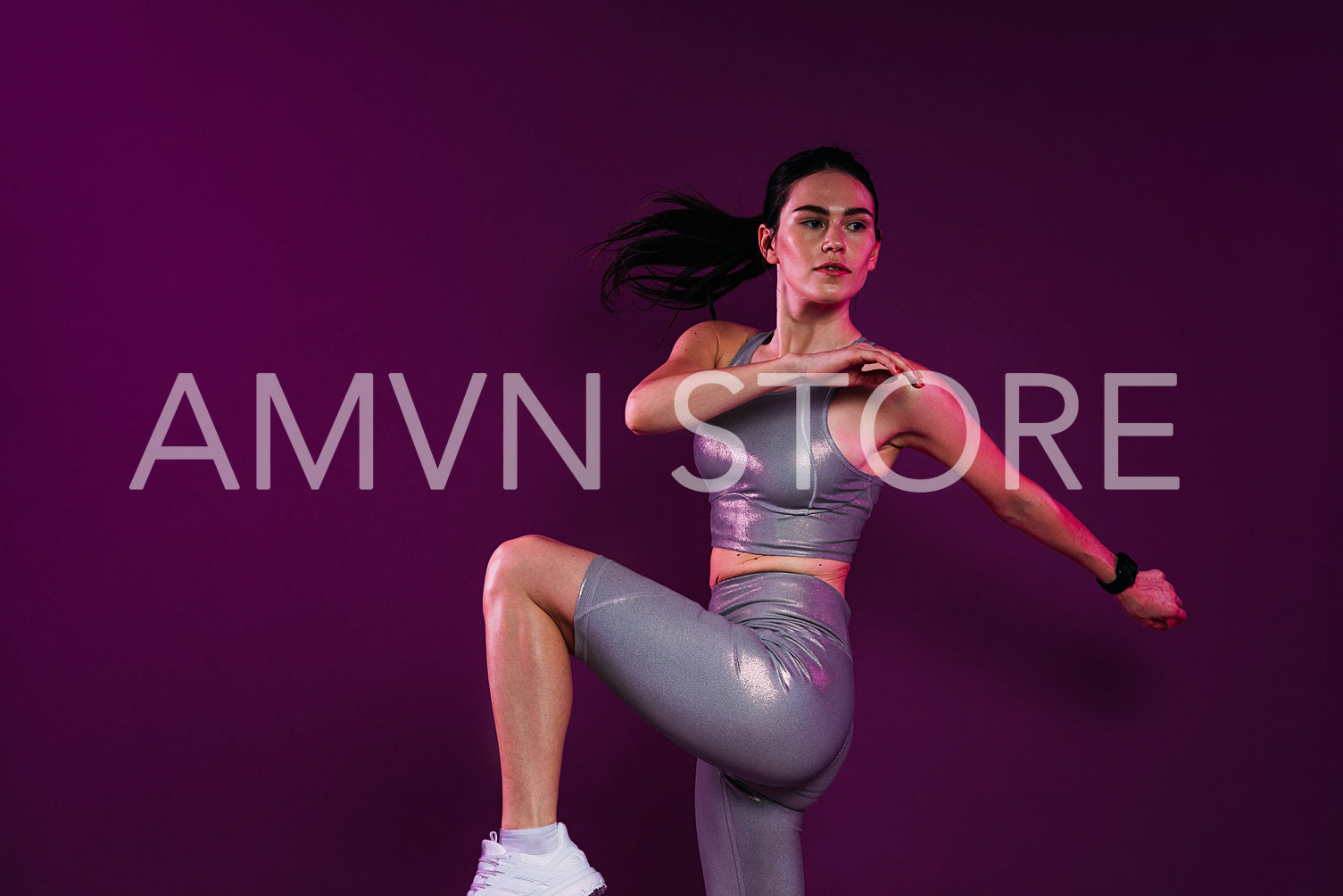 Young slim woman in silver sportrswear warming up her body over magenta backdrop