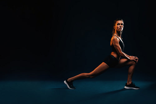 Side view of fit woman stretching legs. Caucasian female working out on black background.