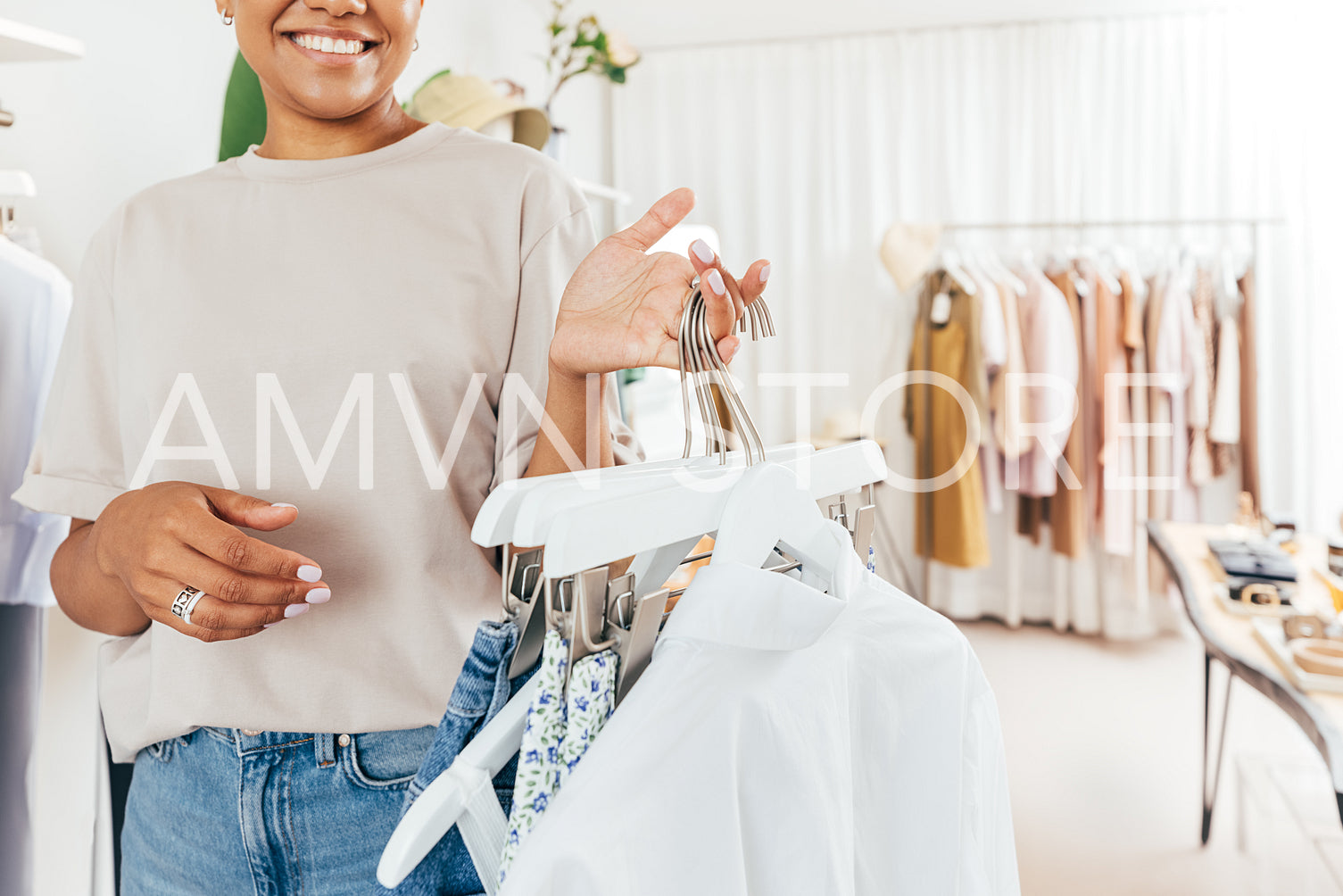 Cropped shot of a smiling woman working in a boutique, holding hangers with clothes