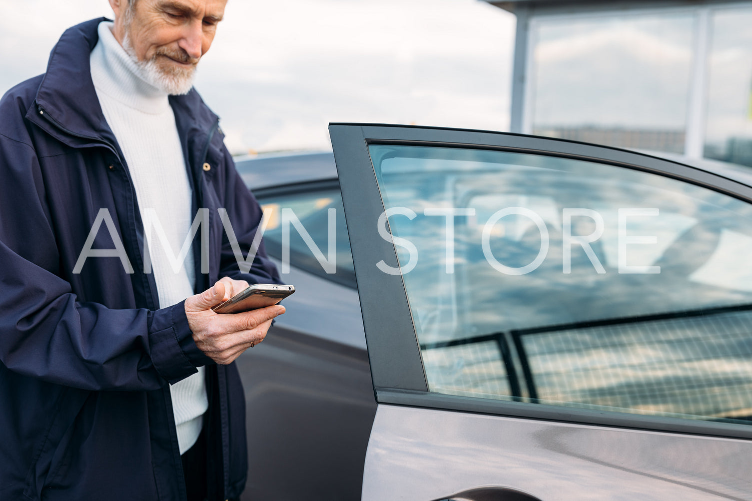 Senior man typing on cell phone while standing at rental car	