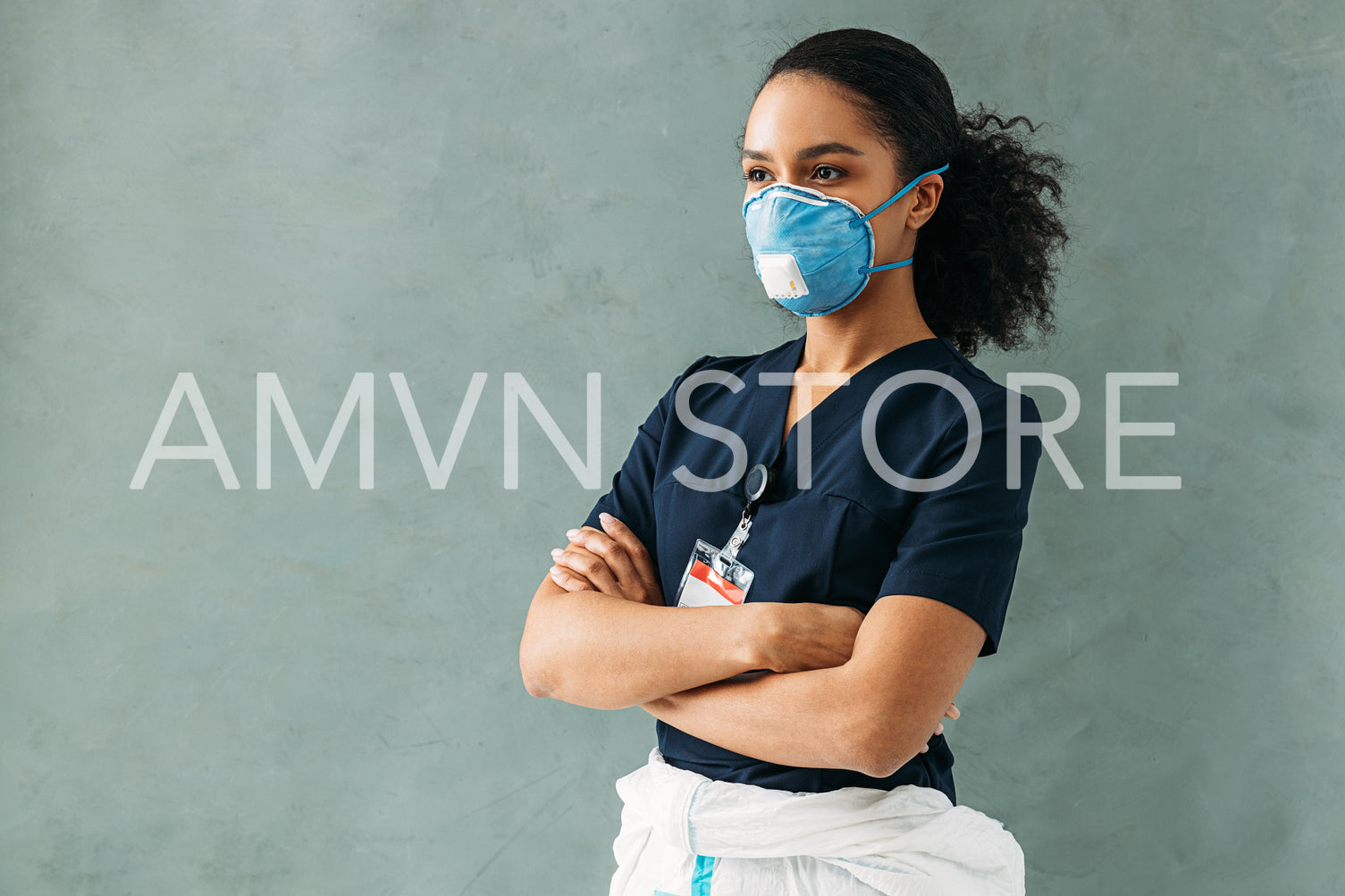 Young nurse in medical uniform with badge standing at wall with crossed arms	