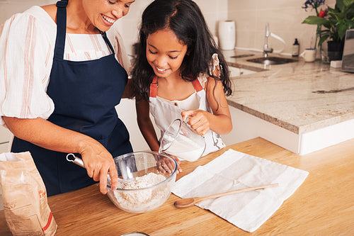 Girl pouring milk into a glass bowl. Grandma and a granddaughter preparing the dough.