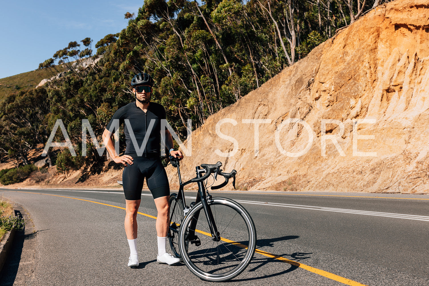 Professional cyclist in black sportswear with his road bike looking at a camera while standing on an empty road