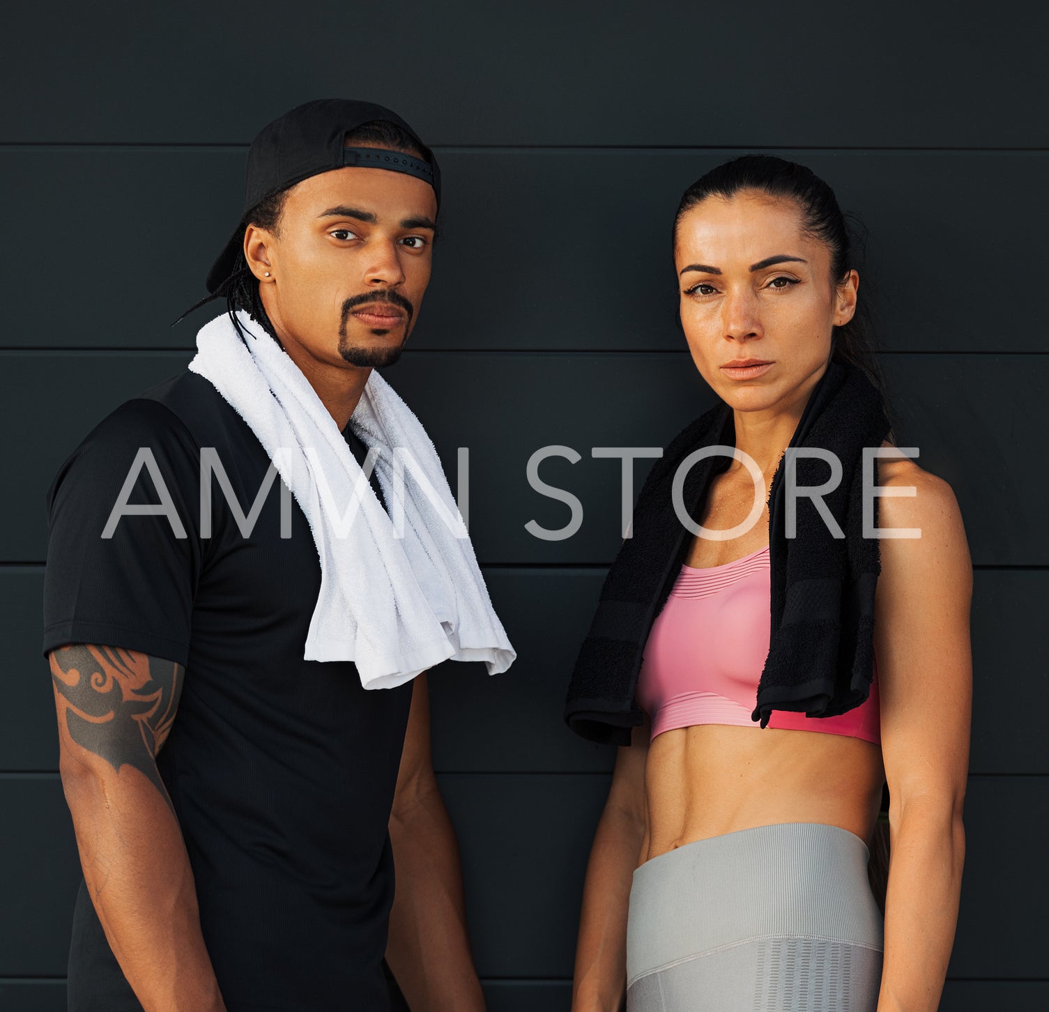 Two young athletes at a black wall. Fitness couple with towels relaxing at a wall.