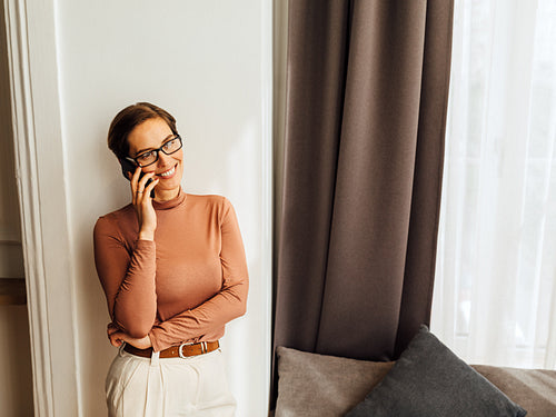 High angle view of caucasian businesswoman leaning a wall in apartment and talking on mobile phone