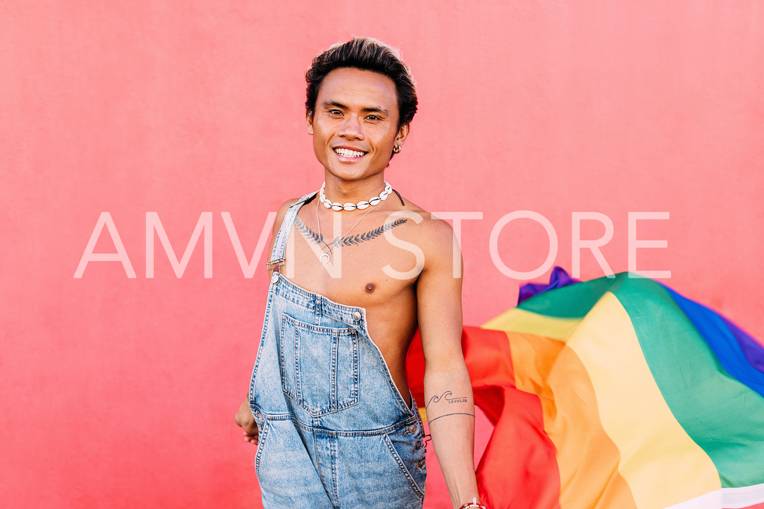 Smiling guy holding a rainbow LGBT flag while standing against a pink wall outdoors