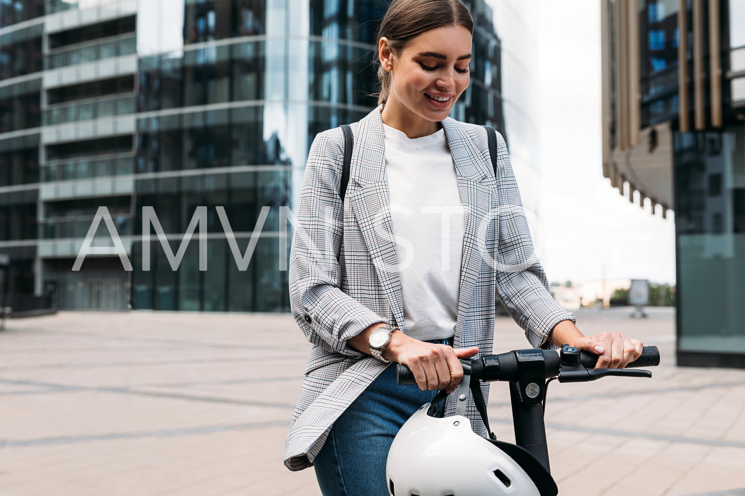 Smiling blond woman holding a handlebar of an e-scooter. Female in formal wear standing on electric push scooter ready to ride.