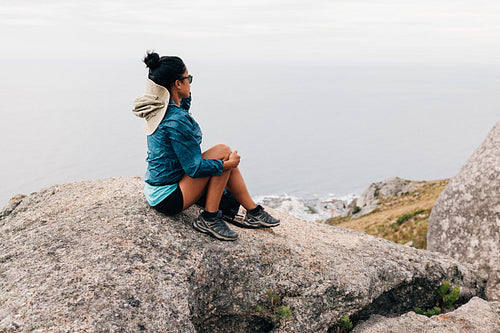 Rear view of woman sitting on the cliff looking at the view during hike