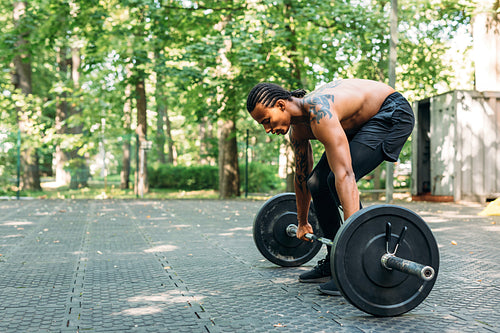 Side view of bare-chest athlete with a barbell. Sportsman preparing for deadlifting.