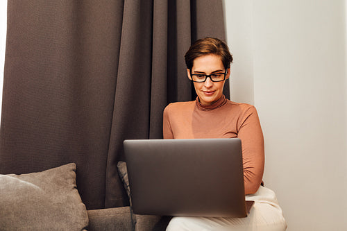 Caucasian woman in formal clothes sitting on sofa in hotel room and looking on laptop screen