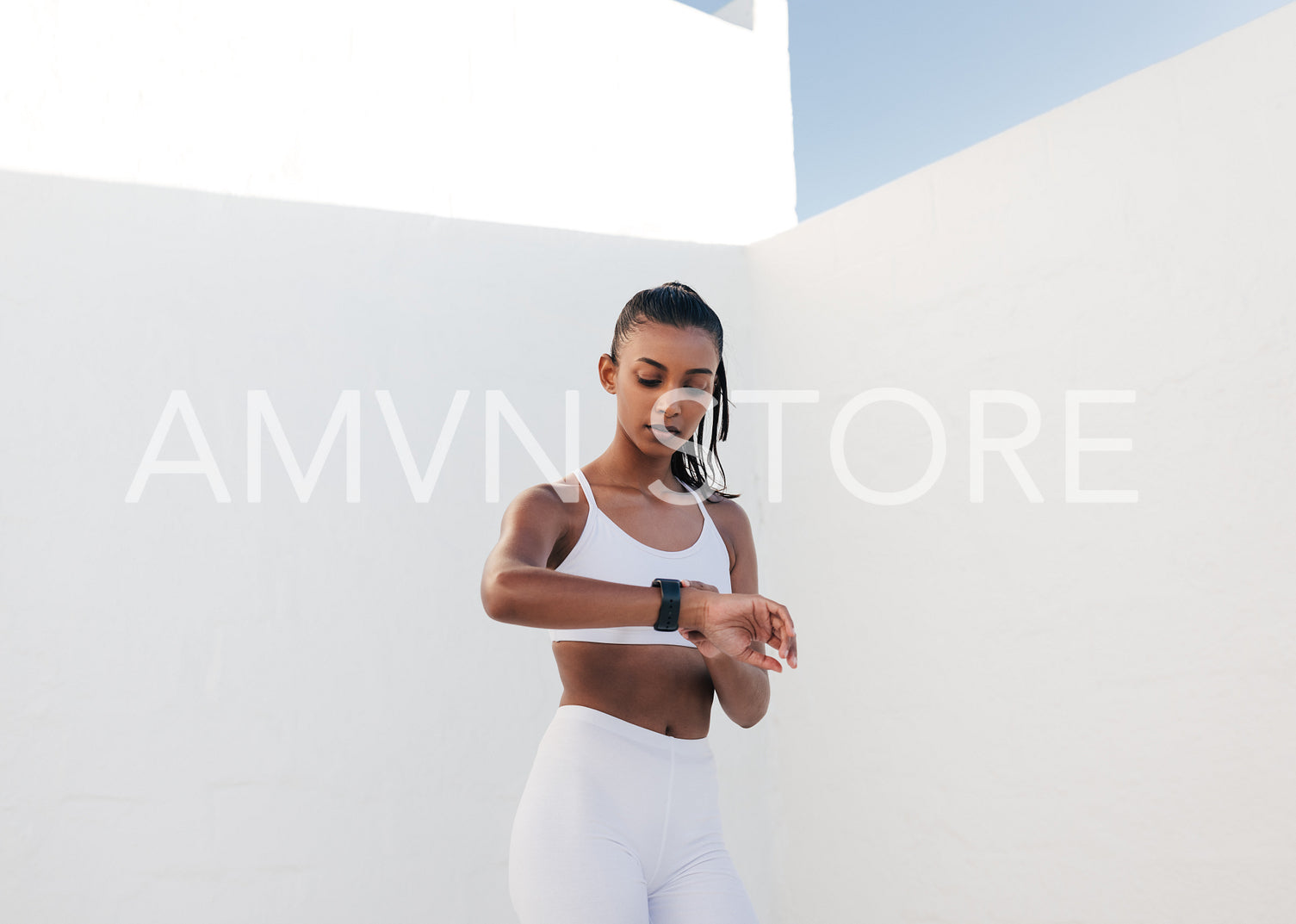 Young slim woman checking heart rate in the white outdoor studio. Fitness female looking at smartwatch checking pulse.