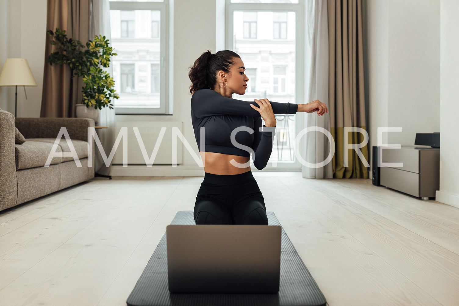 Young woman repeating exercises while watching online exercise session on her laptop in the living room	