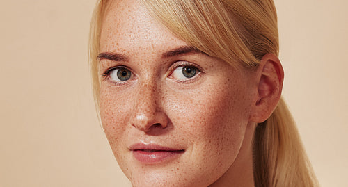 Close-up detailed portrait of a beautiful blond woman with freckled skin. Young female with freckles against a beige backdrop.