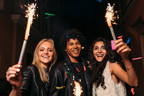 Young man and women having fun at night street with sparklers and confetti