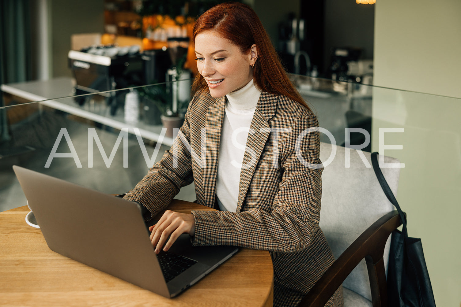 Smiling woman entrepreneur with ginger hair wearing blazer typing on laptop in the cafe