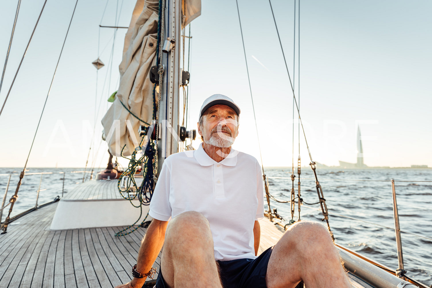 Relaxed mature man sitting on his yacht. Yachtsman resting on the boat at sunset and looking away.	