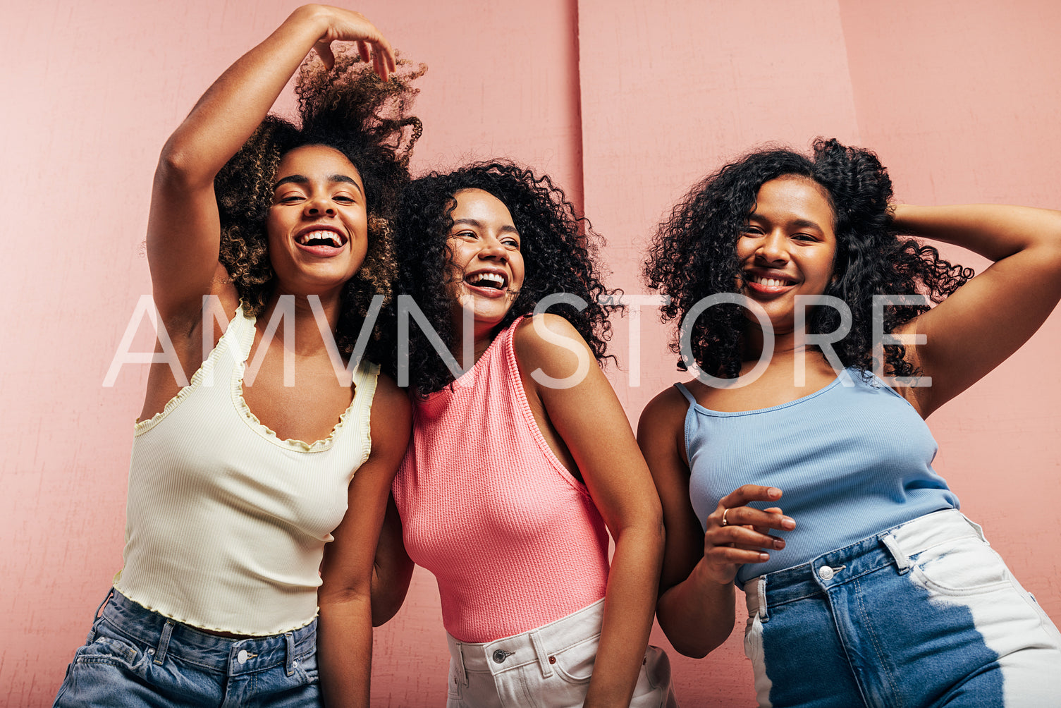 Three young women in bright casuals dancing together at a pink wall and having fun