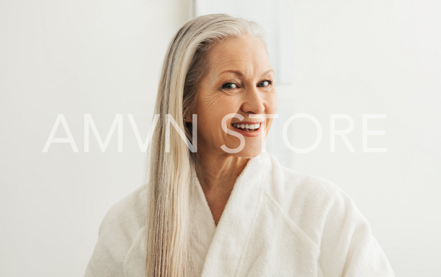 Cheerful female with gray hair in a bathrobe looking at her reflection