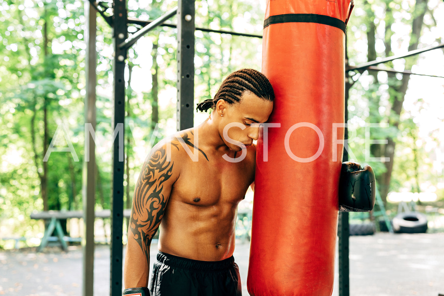 Exhausted kickboxer leaning on a punching bag outdoors. Young boxer resting during a workout on the sports ground.