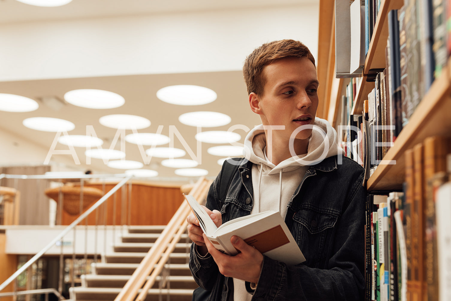 Young student with book looking at bookshelf. Teenager in library reading a book.