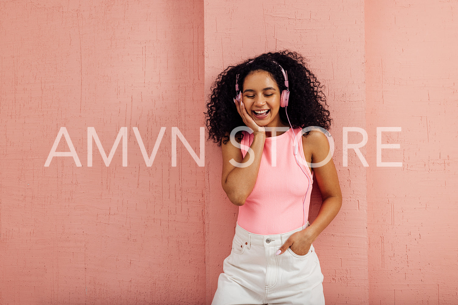 Cheerful woman listening to music leaning pink wall with closed eyes