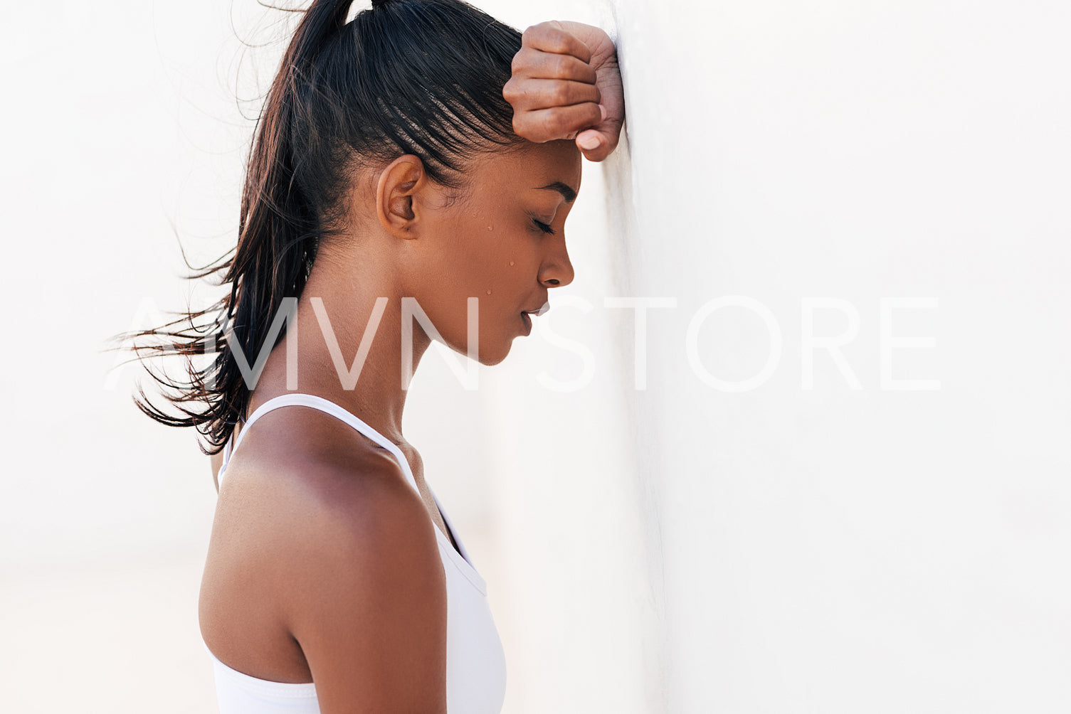 Female with drops of sweat on her face relaxing a white wall with closed eyes