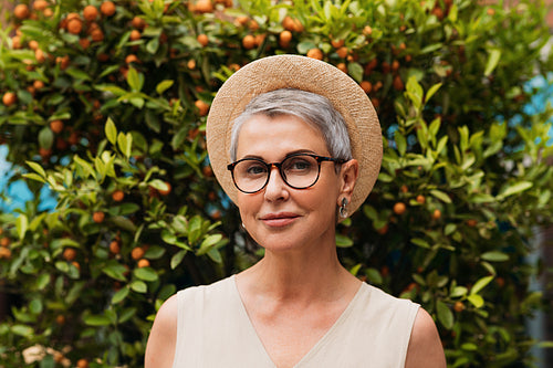 Portrait of a stylish mature woman. Senior female with gray hair wearing glasses and a small straw hat.