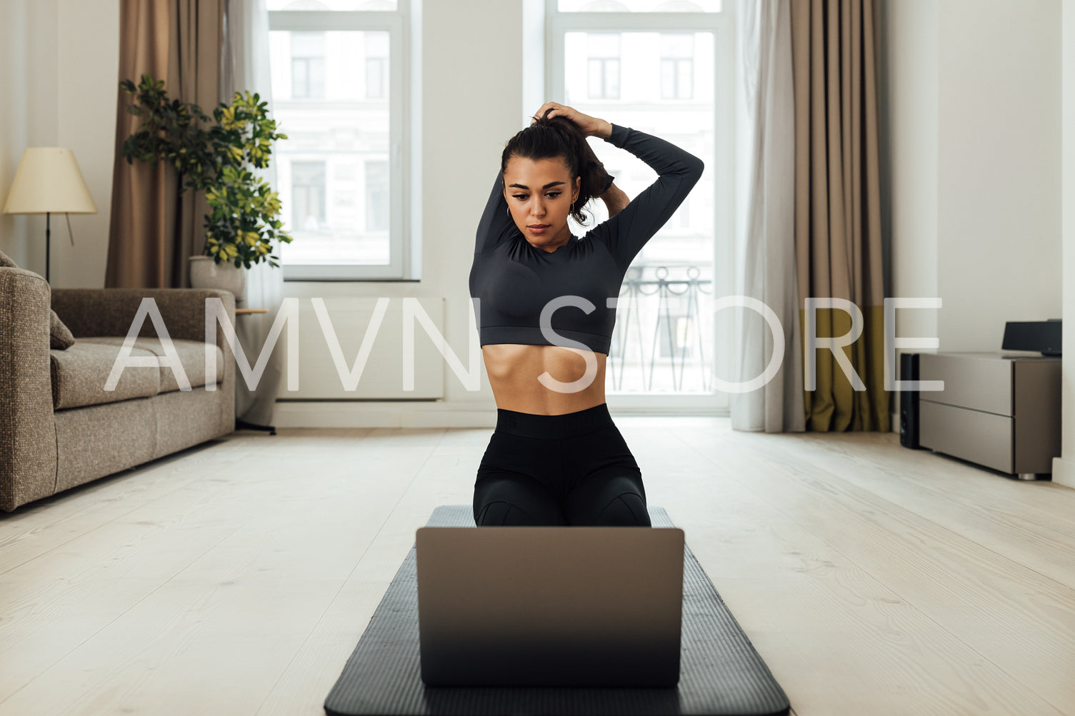 Young woman repeating exercises while watching online exercise session on her laptop in the living room	