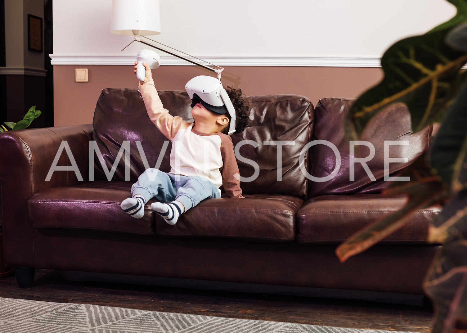 Little boy in comfy clothes using VR set while sitting on a sofa. Kid raising hand with a joystick.