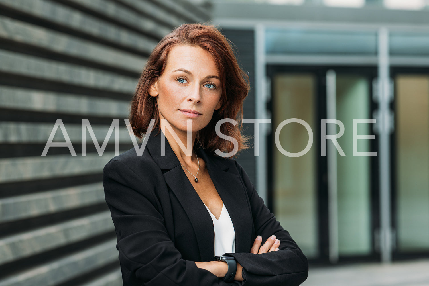 Portrait of a confident businesswoman with ginger hair. Middle-aged businesswoman standing with crossed arms outdoors.