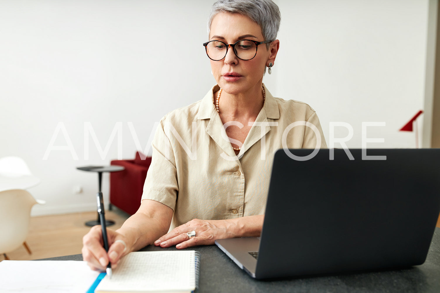 Mature woman writing on a note pad while using laptop computer at home