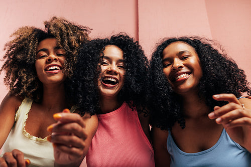 Three happy girlfriends with curly hair laughing together and looking at camera