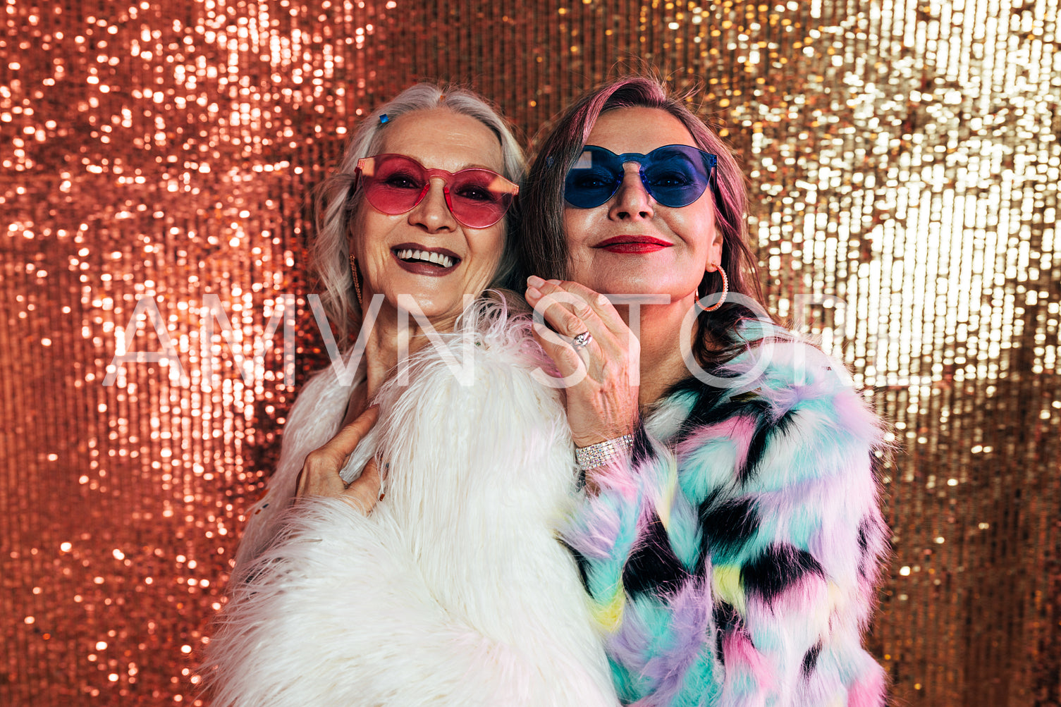 Two smiling senior women in fur coats posing together in studio