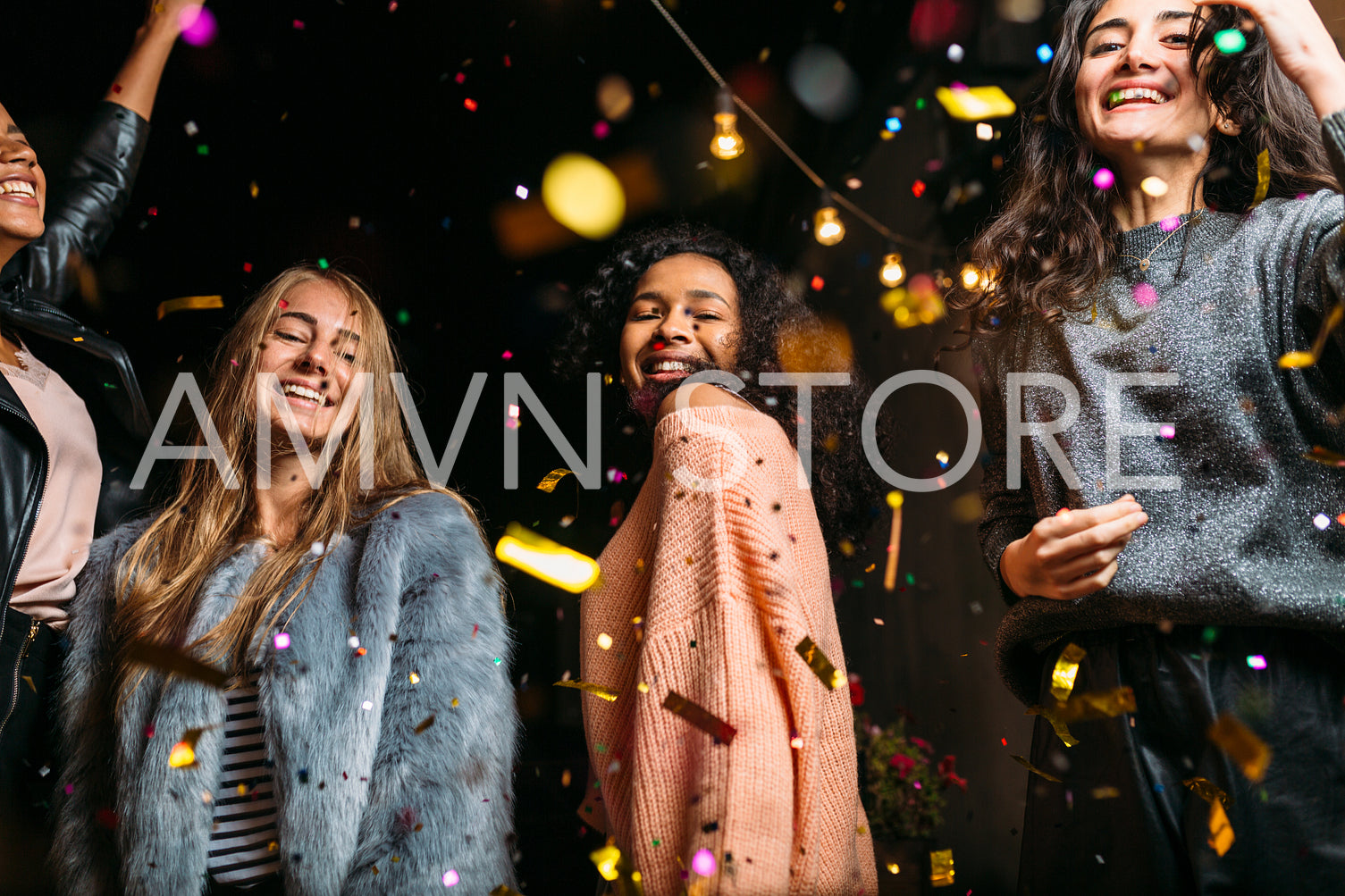 Female friends dancing under confetti at night, looking at camera	